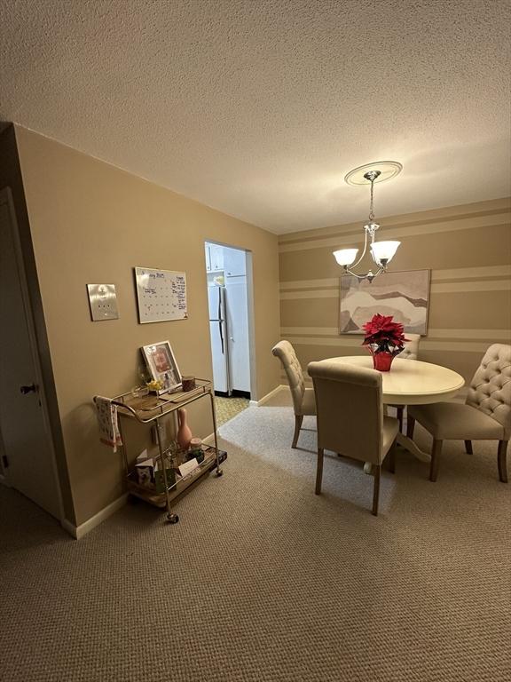 dining space featuring a textured ceiling, a chandelier, and carpet