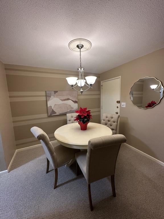 dining area featuring a textured ceiling, an inviting chandelier, and carpet