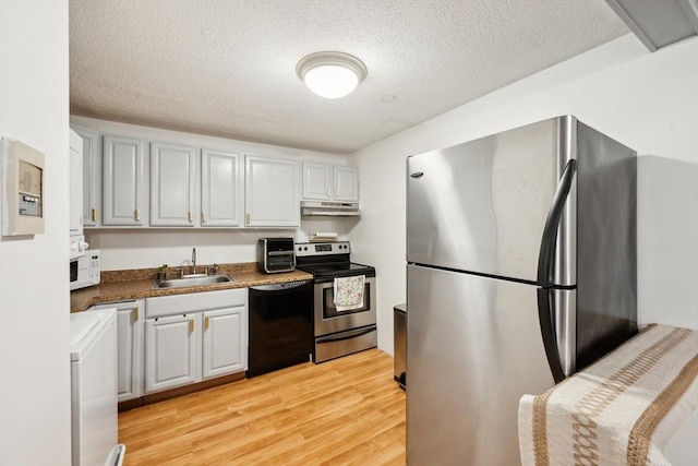 kitchen with under cabinet range hood, a sink, appliances with stainless steel finishes, light wood-type flooring, and washer / dryer