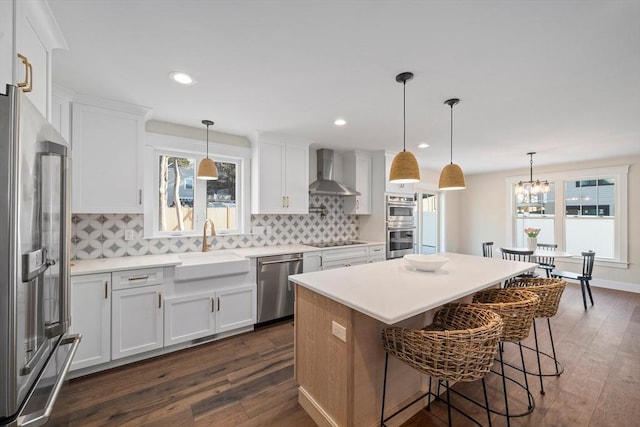 kitchen with wall chimney exhaust hood, hanging light fixtures, white cabinetry, appliances with stainless steel finishes, and sink