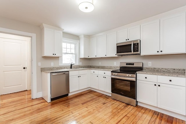 kitchen with sink, stainless steel appliances, light stone countertops, white cabinets, and light wood-type flooring