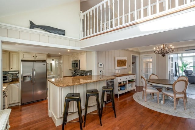 kitchen with cream cabinetry, light stone countertops, wood finished floors, a notable chandelier, and stainless steel appliances