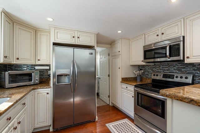 kitchen with light stone counters, cream cabinets, stainless steel appliances, and wood finished floors