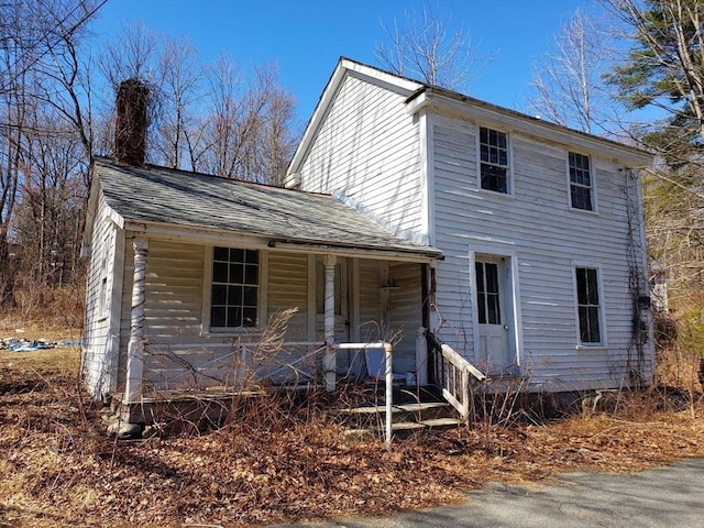 view of front facade with covered porch, a chimney, and roof with shingles