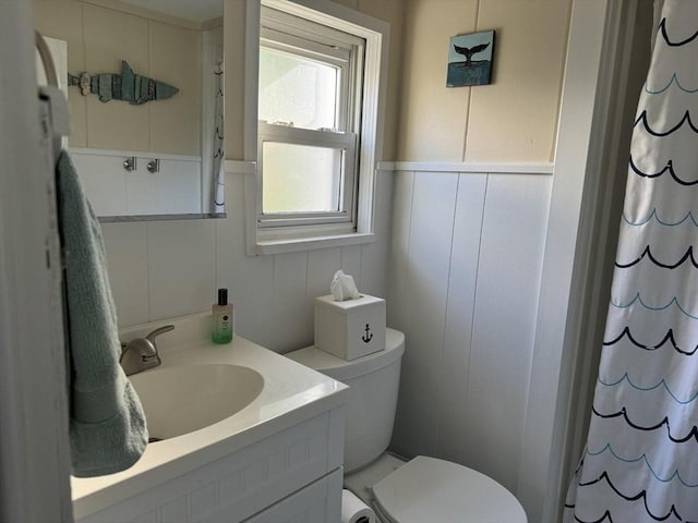 full bath featuring a wainscoted wall, toilet, a shower with shower curtain, a decorative wall, and vanity