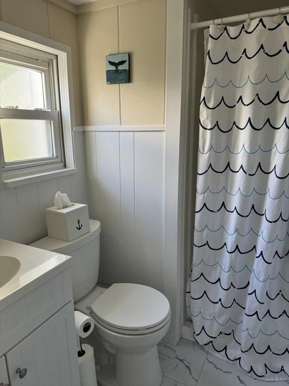 full bath with toilet, a shower with curtain, a decorative wall, marble finish floor, and vanity