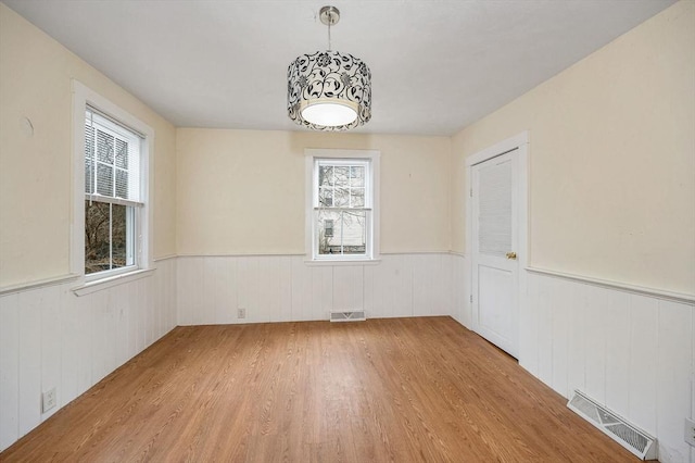 empty room featuring light wood-type flooring, visible vents, and wainscoting