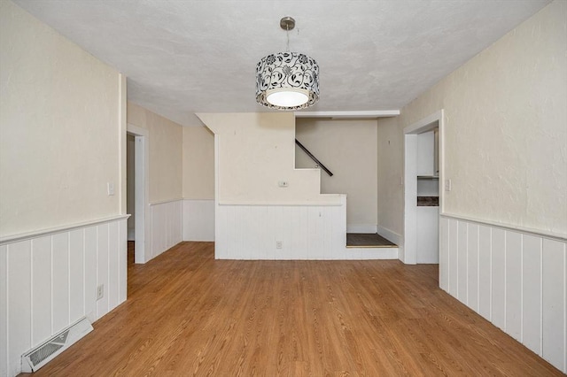 empty room featuring visible vents, wood finished floors, and a wainscoted wall