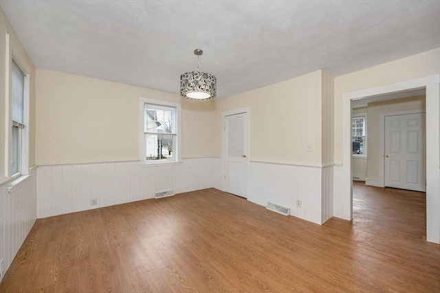 unfurnished room featuring a notable chandelier, visible vents, wainscoting, and wood finished floors