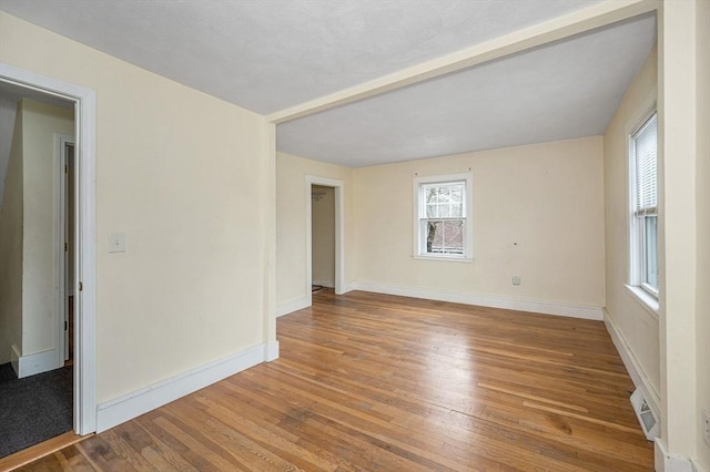 empty room featuring wood finished floors, visible vents, and baseboards