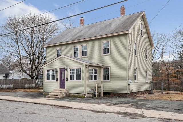 colonial inspired home featuring entry steps, a chimney, and fence