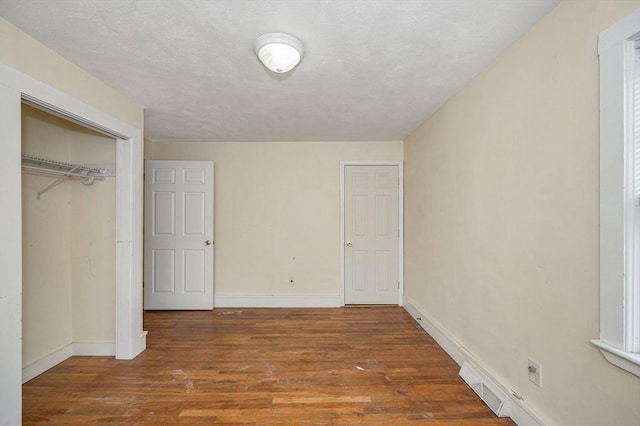 unfurnished bedroom with wood finished floors, visible vents, a closet, and baseboards