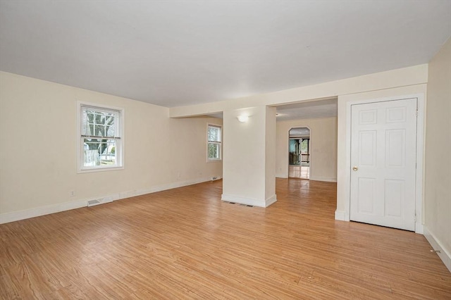 empty room featuring arched walkways, visible vents, baseboards, and light wood-style floors