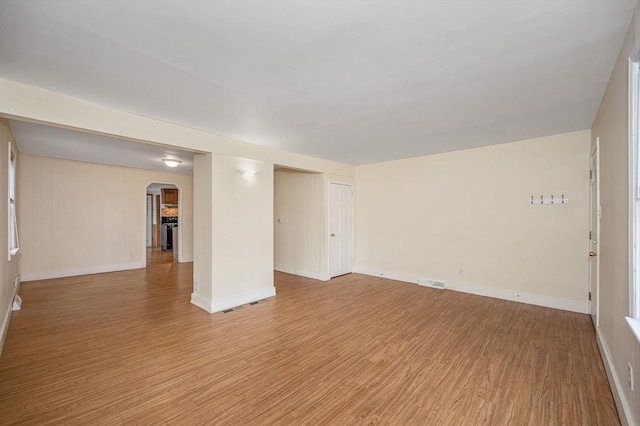 unfurnished room with visible vents, arched walkways, light wood-style floors, and baseboards