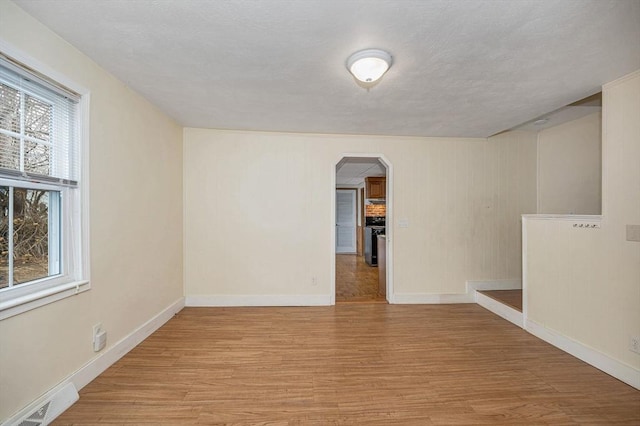 unfurnished room with wood finished floors, visible vents, baseboards, arched walkways, and a textured ceiling