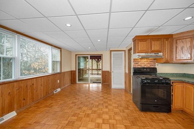 kitchen with gas stove, visible vents, wainscoting, wood walls, and under cabinet range hood