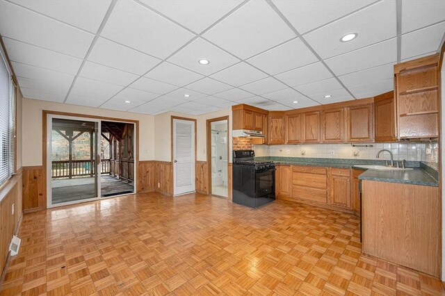 kitchen with a wainscoted wall, black gas stove, open shelves, and a sink