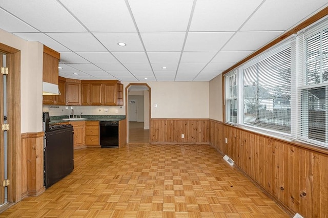 kitchen with wooden walls, visible vents, arched walkways, black appliances, and wainscoting