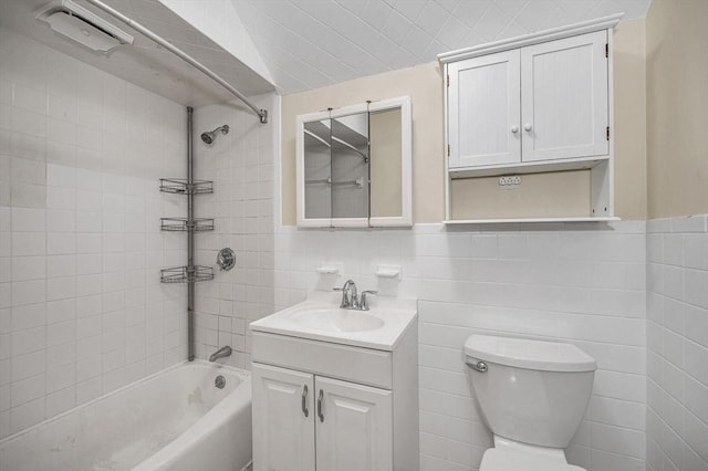 bathroom featuring toilet, vanity, tile walls, and shower / bathing tub combination