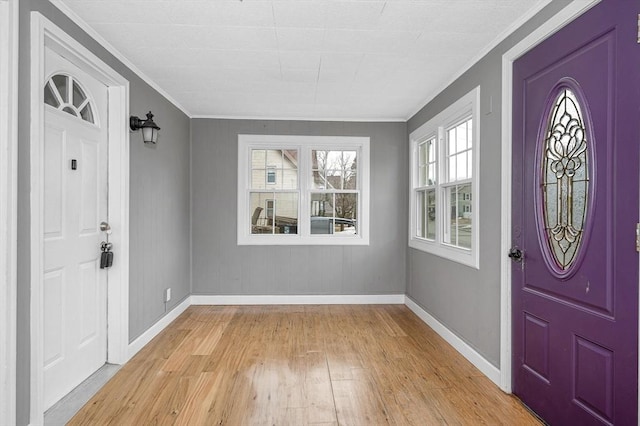 foyer entrance featuring baseboards, crown molding, and light wood finished floors