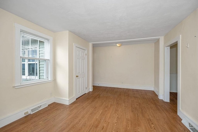 empty room with light wood-style floors, visible vents, and baseboards