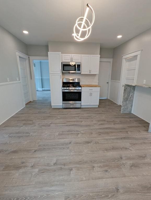 16 Horton St Unit 2, Salem, MA 01970 - kitchen with appliances with stainless steel finishes, white cabinetry, light wood-type flooring, pendant lighting, and wainscoting