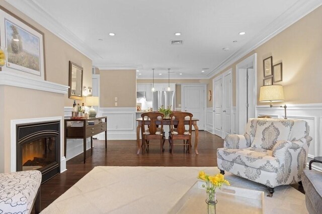 living area with visible vents, a wainscoted wall, dark wood-style floors, a glass covered fireplace, and a decorative wall