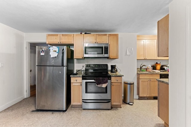 kitchen with a sink, dark stone counters, appliances with stainless steel finishes, and light brown cabinets