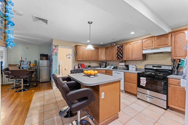 kitchen featuring under cabinet range hood, a kitchen island, freestanding refrigerator, dishwasher, and stainless steel range with gas stovetop