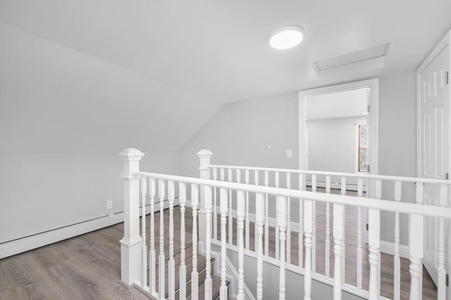 hall with an upstairs landing, wood finished floors, attic access, and a baseboard heating unit