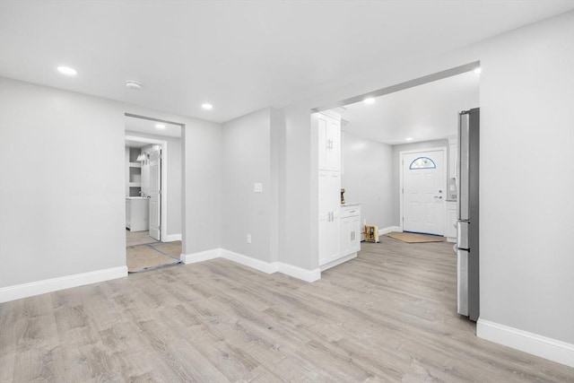below grade area with light wood-style floors, freestanding refrigerator, baseboards, and recessed lighting