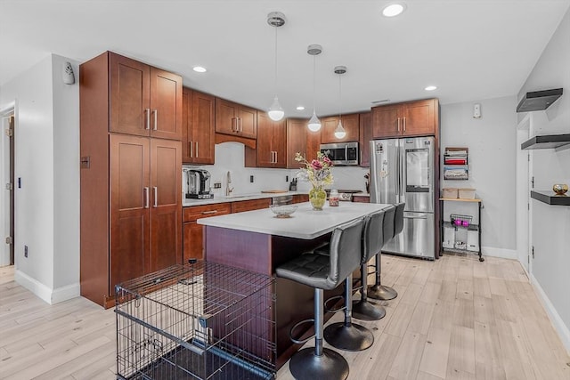 kitchen with a sink, light wood-type flooring, light countertops, baseboards, and appliances with stainless steel finishes