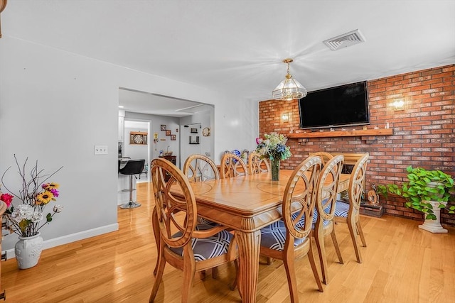 dining space with light wood-type flooring, baseboards, visible vents, and brick wall