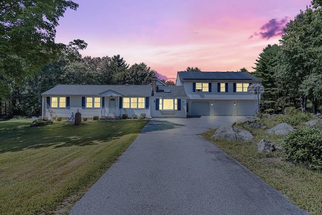 view of front facade with a chimney, a front lawn, driveway, an attached garage, and roof mounted solar panels