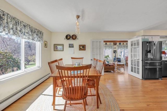 dining space featuring a baseboard radiator, french doors, and light wood finished floors