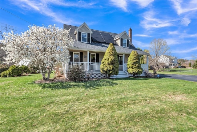 cape cod house featuring a front lawn, covered porch, a chimney, and solar panels
