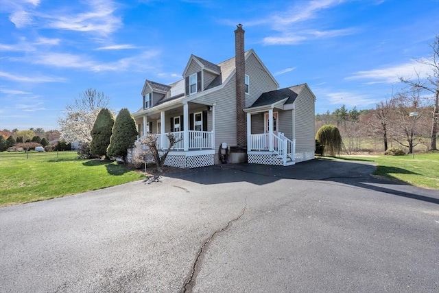 view of side of home featuring a lawn, aphalt driveway, covered porch, and a chimney