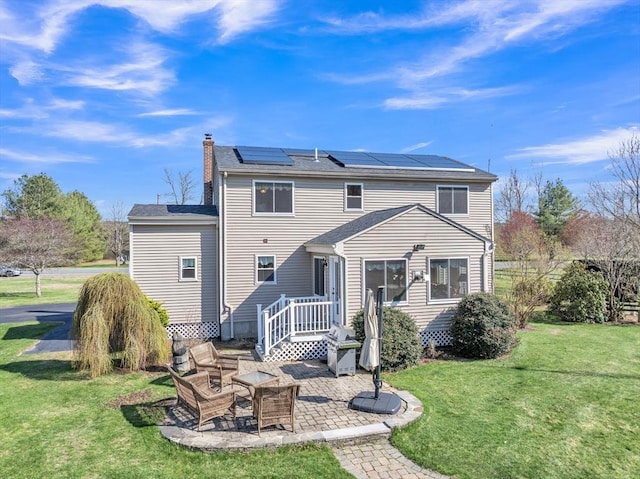 rear view of house featuring a chimney, solar panels, a patio area, a lawn, and a fire pit
