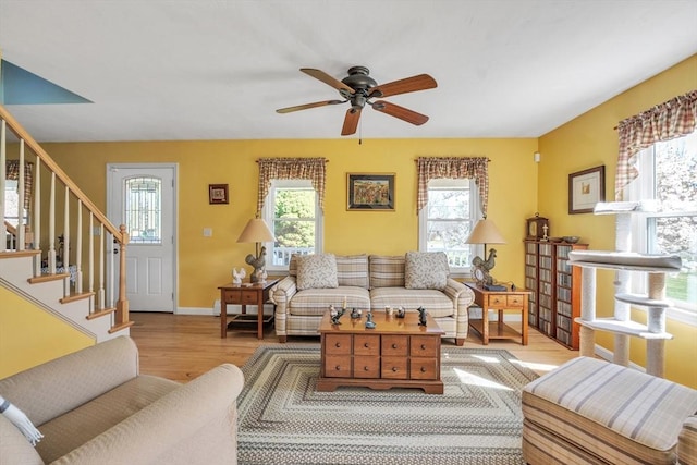 living area with stairs, ceiling fan, wood finished floors, and a healthy amount of sunlight