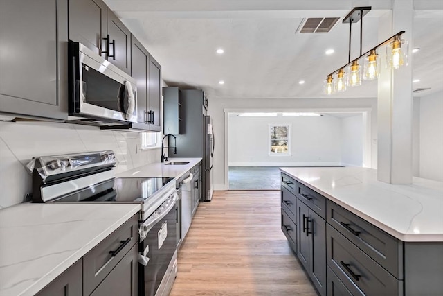 kitchen featuring light stone countertops, gray cabinetry, stainless steel appliances, decorative light fixtures, and light hardwood / wood-style floors