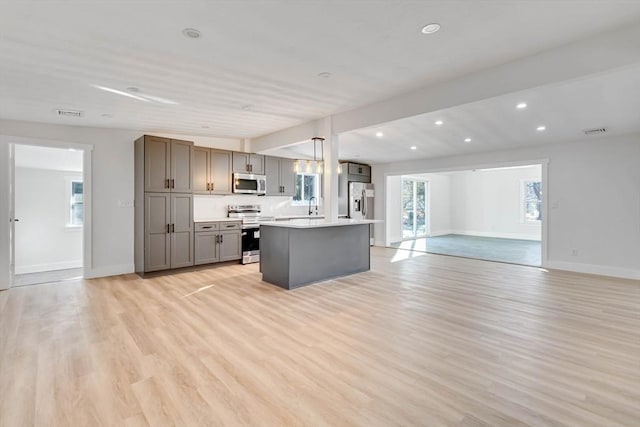 kitchen featuring appliances with stainless steel finishes, light hardwood / wood-style floors, pendant lighting, gray cabinets, and a kitchen island