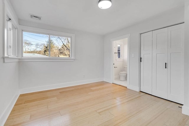 unfurnished bedroom with light wood-type flooring, ensuite bath, and a closet