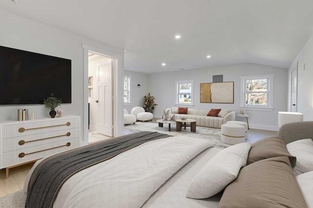 bedroom with light wood-type flooring, ensuite bath, multiple windows, and lofted ceiling