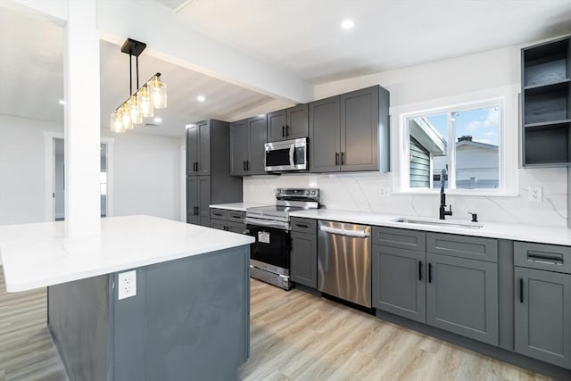 kitchen with gray cabinetry, a center island, sink, appliances with stainless steel finishes, and decorative light fixtures