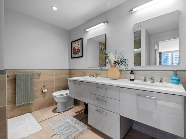 bathroom with double vanity, toilet, tile walls, and a sink