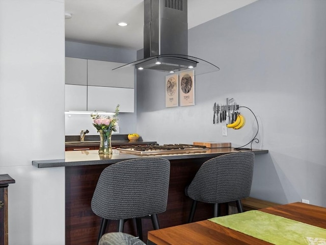 kitchen featuring dark countertops, island range hood, a breakfast bar area, stainless steel gas stovetop, and a sink