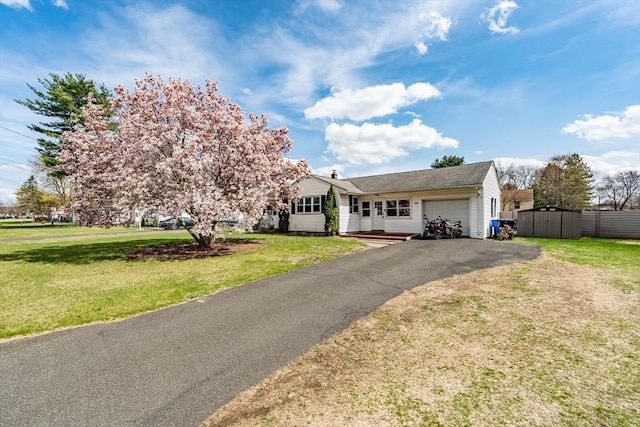 ranch-style house featuring an attached garage, a front lawn, and aphalt driveway