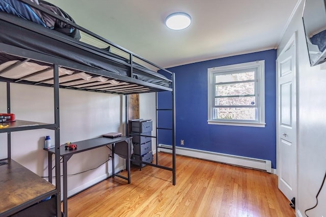 bedroom with a baseboard heating unit, baseboards, ornamental molding, and wood finished floors