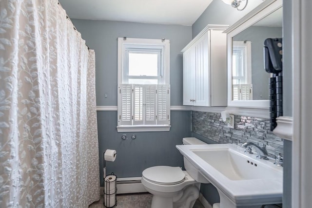 bathroom featuring tile patterned floors, backsplash, toilet, a sink, and baseboards