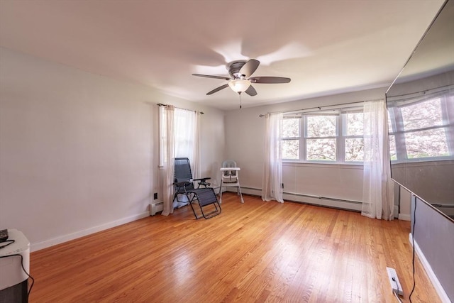 interior space with a baseboard heating unit, ceiling fan, a wealth of natural light, and light wood-type flooring